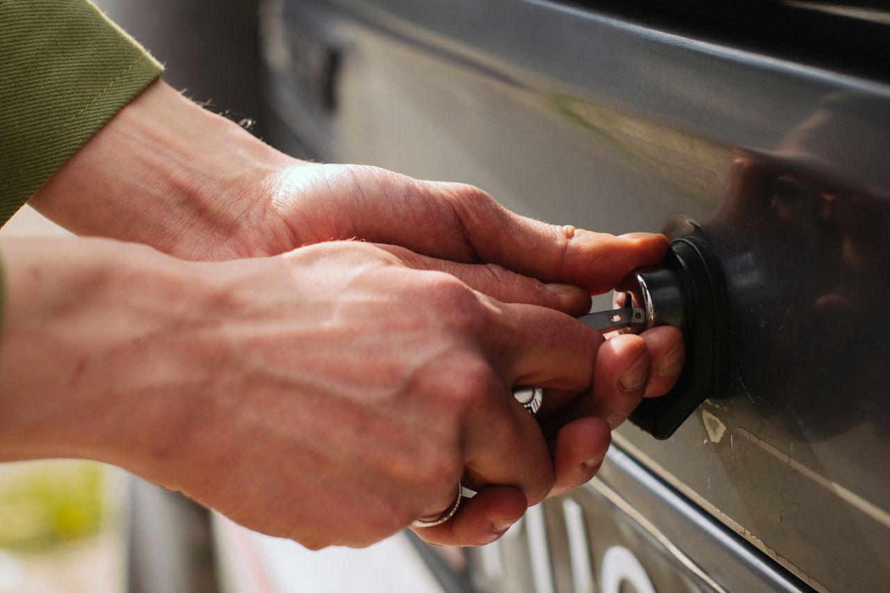 About Close-up of hands unlocking a vehicle trunk with a key, showing detail and reflection.