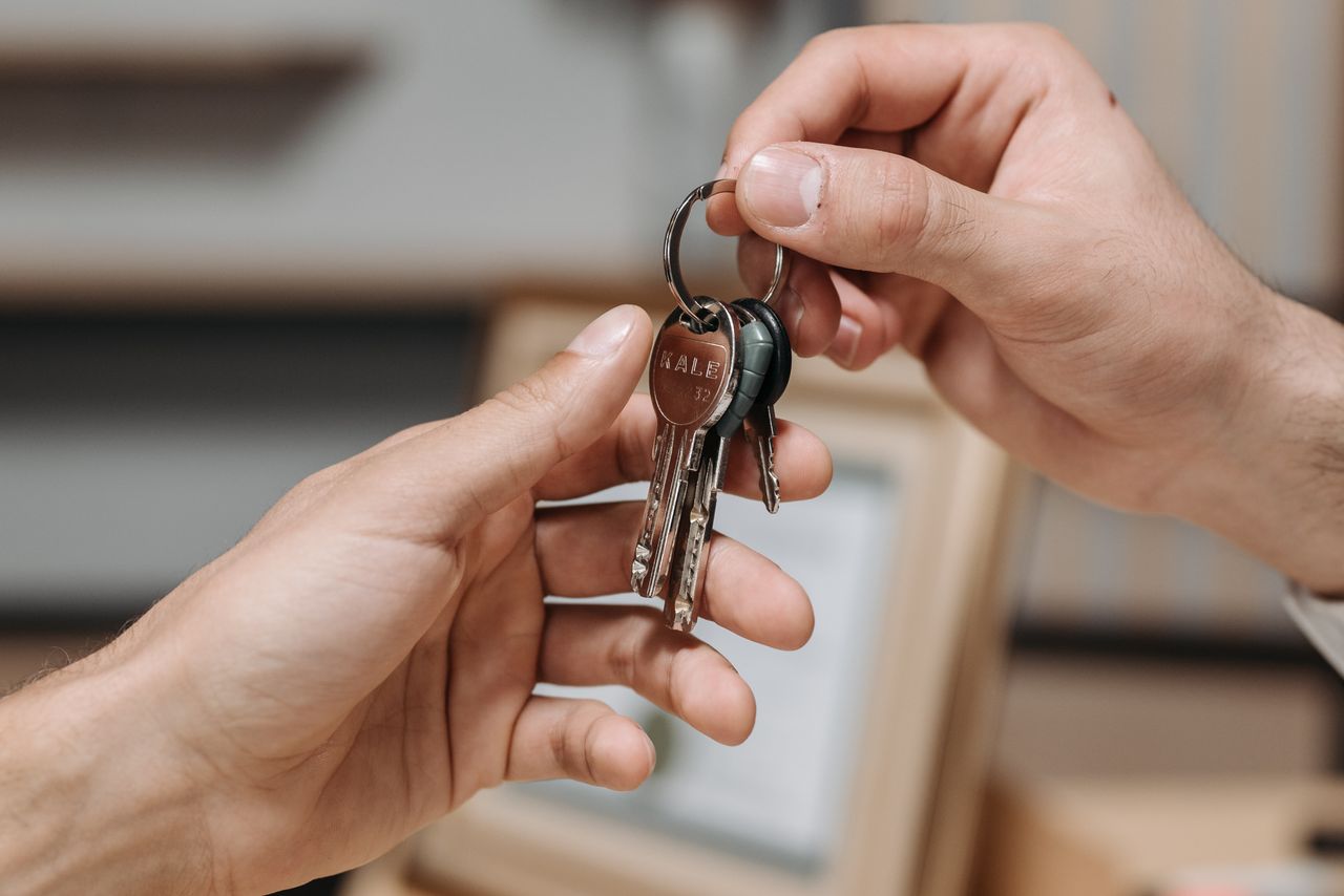 A close-up image of two hands exchanging a set of keys indoors.